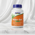 Supplement bottle labeled 'Water Out' on a marble surface with white curtain background